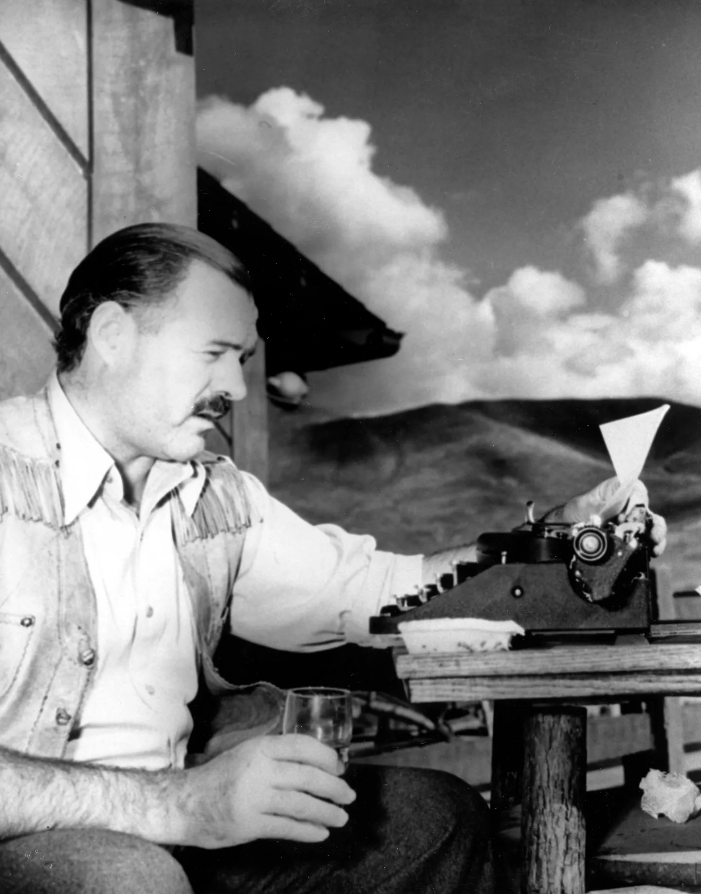 Ernest Hemingway at his typewriter, drink in hand